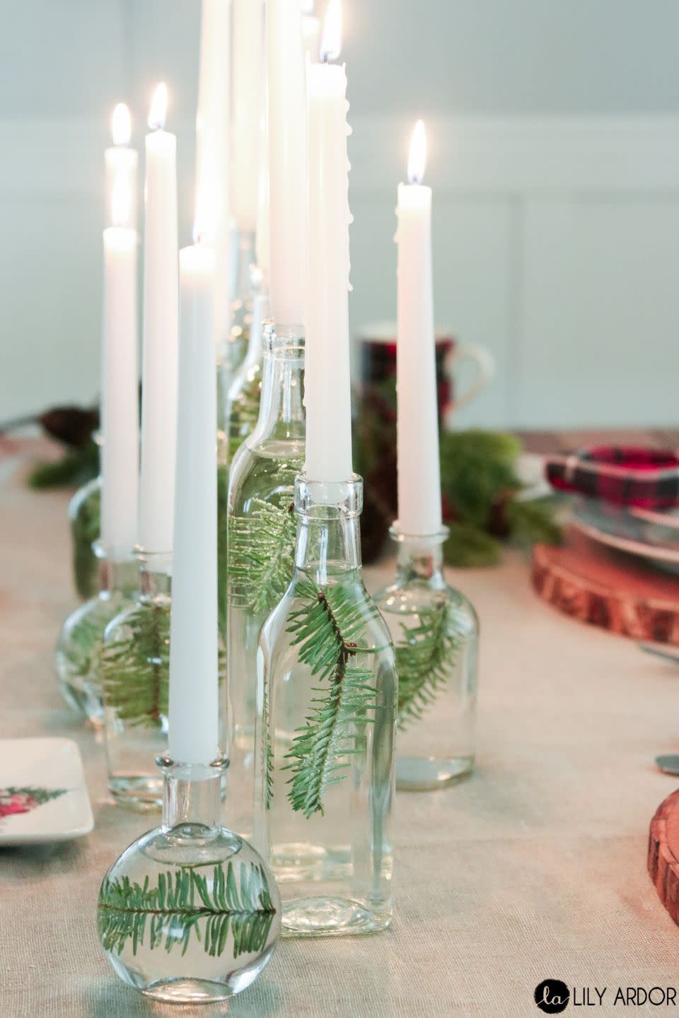 small glass bottles are filled with water and a single pine branch, then topped with a candle the centerpiece is a great baby shower idea