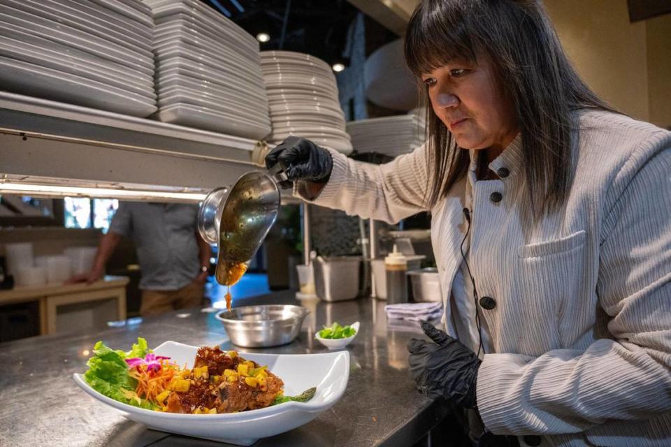 Wan Phen “Penny” Mufuka, co-owner and chef at Bamboo Penny’s, pours a house-made mango sauce over a mango duck dish.