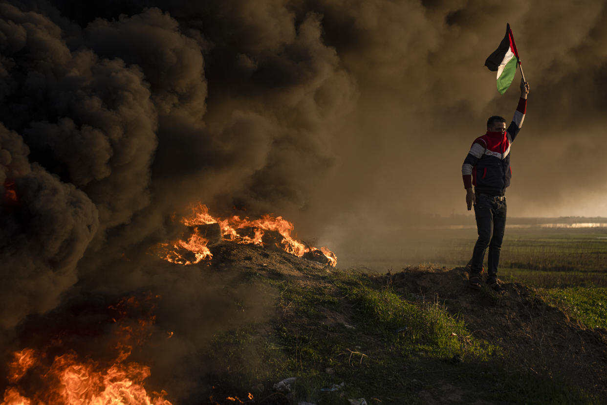 A Palestinian demonstrator waves a national flag near burning tires, protesting against an Israeli military raid in the West Bank city of Jenin.