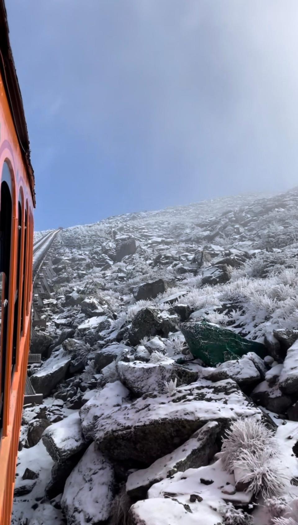 Ice and snow covered rocks and shrubs seen from the window of an orange train