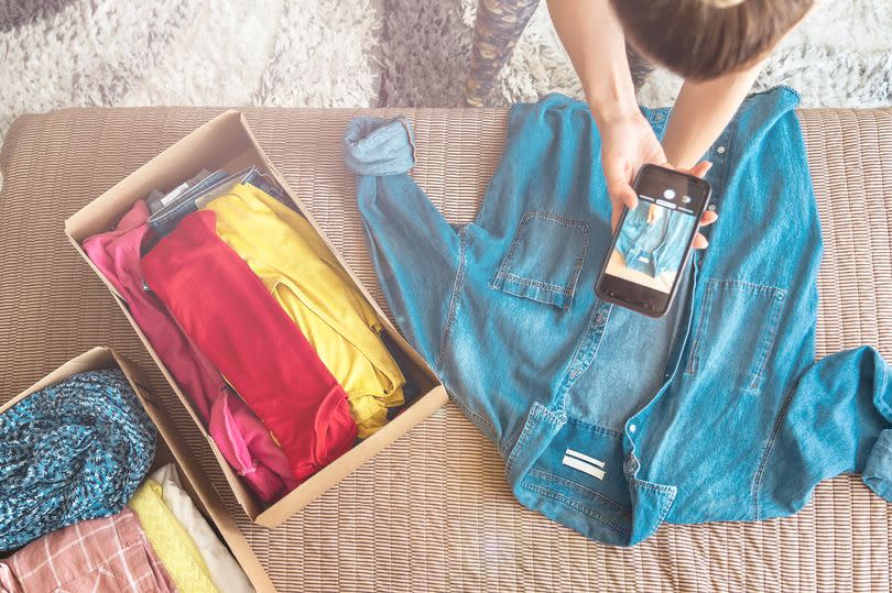 Woman taking photo of denim shirt on smartphone to sell it on internet shop.