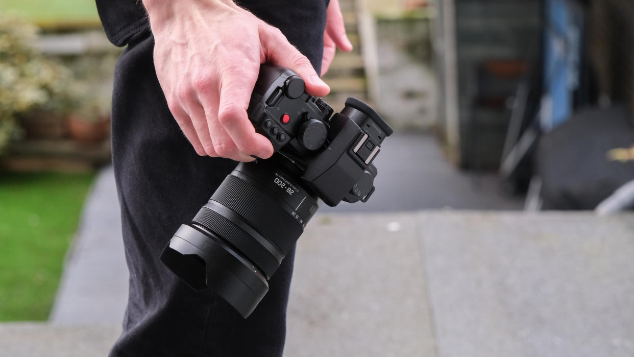  Panasonic Lumix S 28-200mm attached to a camera held in a hand down by a side. 