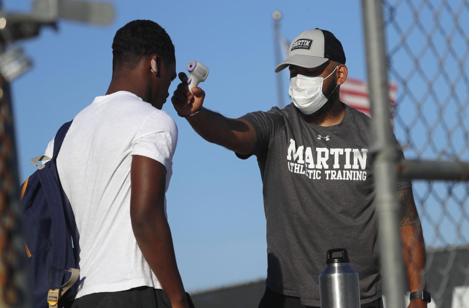 Before entering the field gates for football strength and conditioning camp at Arlington Martin High School, athletic Trainer Joey Pena, right, uses a thermometer on the forehead of sophomore running back Gervawn Neville for a temperature check Thursday, June 18, 2020, in Arlington, Texas. While states have been easing the economic and social lockdowns prompted by the coronavirus pandemic, some are now letting high school athletes return for summer workouts before teachers have even figured out how they are going to hold classroom instruction. (AP Photo/LM Otero)