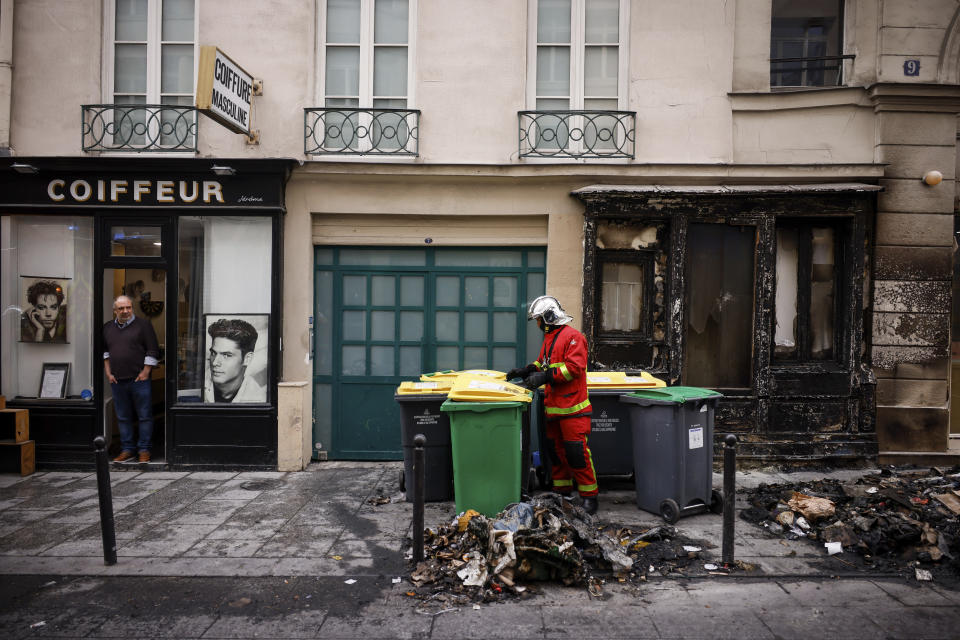 A fireman pushes a waste container among the remains of a garbage fire from last night protests against the retirement bill in Paris, Friday, March 24, 2023. French President Macron's office says state visit by Britain's King Charles III is postponed amid mass strikes and protests. (AP Photo/Thomas Padilla)