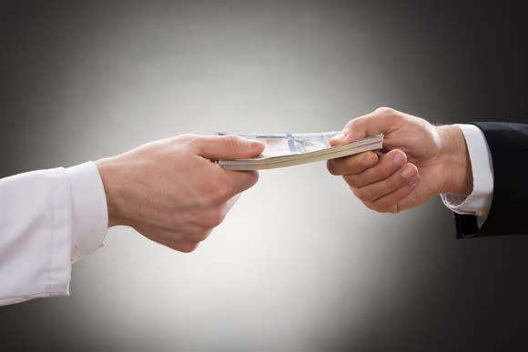 Two men, each holding onto one end of a stack of money.