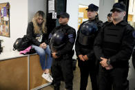 State worker Florencia Ugarte sits on a desk by police blocking her colleagues who were laid-off from entering the National Institute against Discrimination, Xenophobia, and Racism, in Buenos Aires, Argentina, Wednesday, April 3, 2024. During his four months in office, President Javier Milei has closed the Ministry of Women, Gender and Diversity, banned the government’s use of gender-inclusive language and shuttered the National Institute against Discrimination, Xenophobia and Racism. (AP Photo/Natacha Pisarenko)