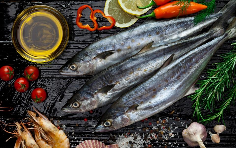 Three raw mackerel fish shot directly above on dark table with seafood and some ingredients for cooking. -  E+/ fcafotodigital