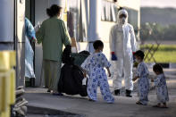 In this photo taken and released by Malaysia's Ministry of Health, a health worker looks at a woman and children arrive at Kuala Lumpur International Airport in Sepang, Malaysia, Wednesday, Feb. 26, 2020, after being evacuated from China's Wuhan, the epicenter of the coronavirus outbreak. U.S. health officials warned Tuesday that the burgeoning coronavirus is certain to spread more widely in the country at some point, even as their counterparts in Europe and Asia scrambled to contain new outbreaks of the illness. (Muzzafar Kasim/Malaysia's Ministry of Health via AP)