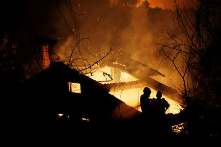 Firefighters try to extinguish a fire in a house as a wildfire burns near the village of Kalamos, north of Athens, Greece, August 13, 2017. REUTERS/Costas Baltas