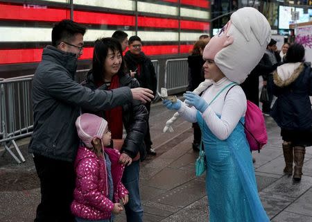 A woman dressed as the character Elsa from the movie Frozen, receives money from tourists after allowing them to take a photograph with her in Times Square, in New York, April 7, 2016. REUTERS/Rickey Rogers