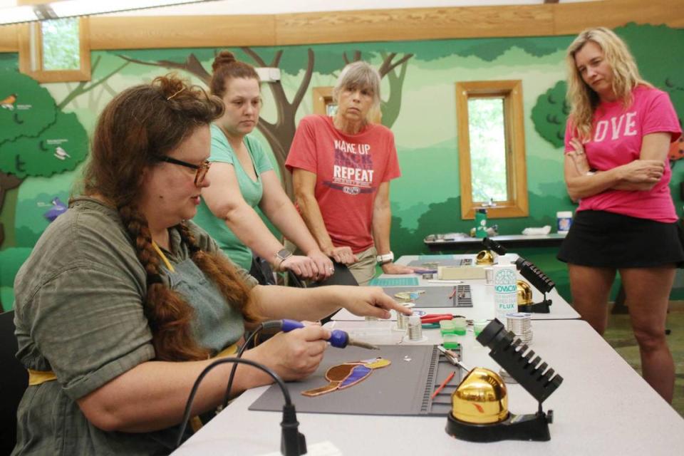 Artist Tara Tonsor demonstrates how to solder stained glass as Amanda Wood, Sandra Campbell and Erika Jump watch during a class at the Overland Park Arboretum.