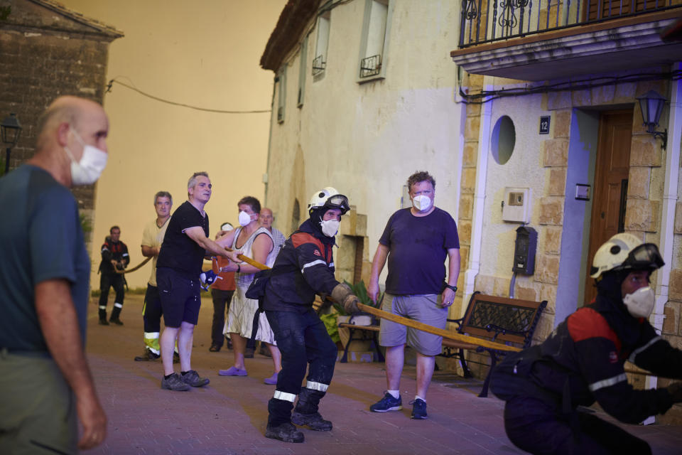 Villagers help firefighters with a hose during a wildfire in Arraiza, northern Spain, Saturday, June 18, 2022. Firefighters in Spain are struggling to contain wildfires in several parts of the country suffering an unusual heat wave for this time of the year. (AP Photo/Sergio Martin)