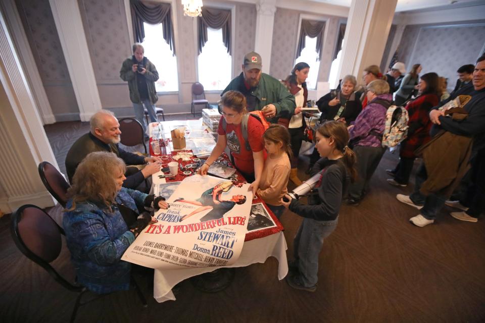 Bailey Kids actor Karolyn Grimes seated at left, signs a movie poster for the Aubin family of Newport, VT; Kevin and Mandy Aubin and their kids Gabriel, 11, and Abigail, 9, during a special autograph signing event at the Gould Hotel during the It's A Wonderful Life Festival in Seneca Falls, NY Friday, Dec. 8, 2023.