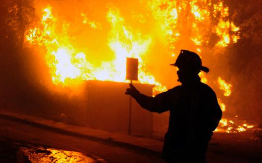 Un bombero en plena tarea cerca de casas en llamas durante un incendio en la ciudad portuaria de Valparaíso, 110 km al oeste de Santiago, Chile, el 12 de abril de 2014. (AFP | Felipe Gamboa)