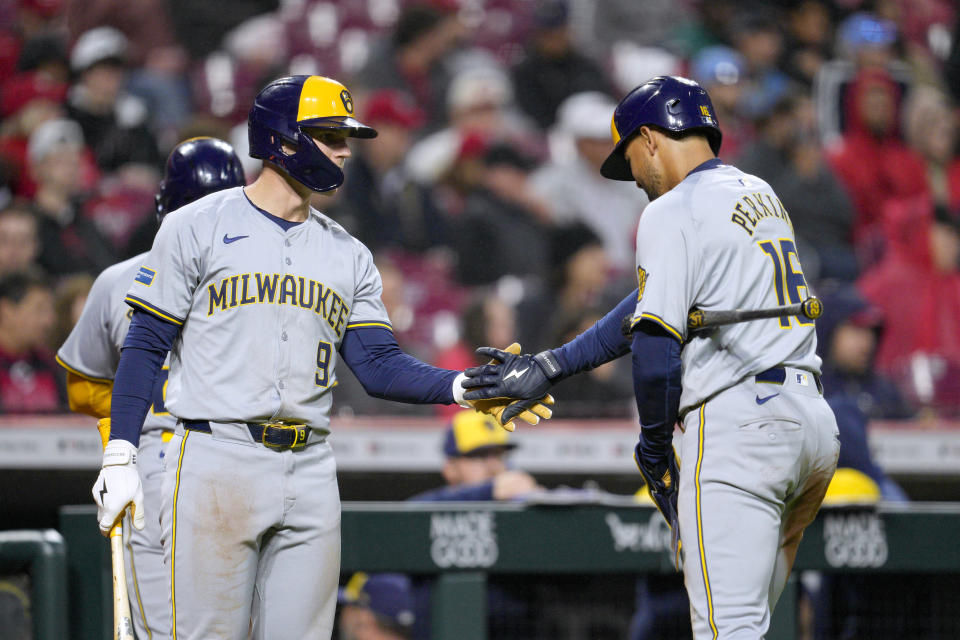 Milwaukee Brewers' Blake Perkins (16) celebrates with Jake Bauers (9) after scoring on a two-run double by Christian Yelich against the Cincinnati Reds during the fifth inning of a baseball game Tuesday, April 9, 2024, in Cincinnati. (AP Photo/Jeff Dean)