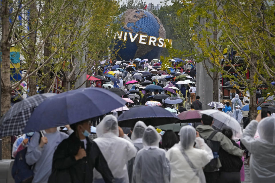 People wearing raincoats and carrying umbrellas walk through a plaza near the entrance of Universal Studios Beijing in Beijing, Monday, Sept. 20, 2021. Thousands of people brave the rain visit to the newest location of the global brand of theme parks which officially opens on Monday. (AP Photo/Andy Wong)