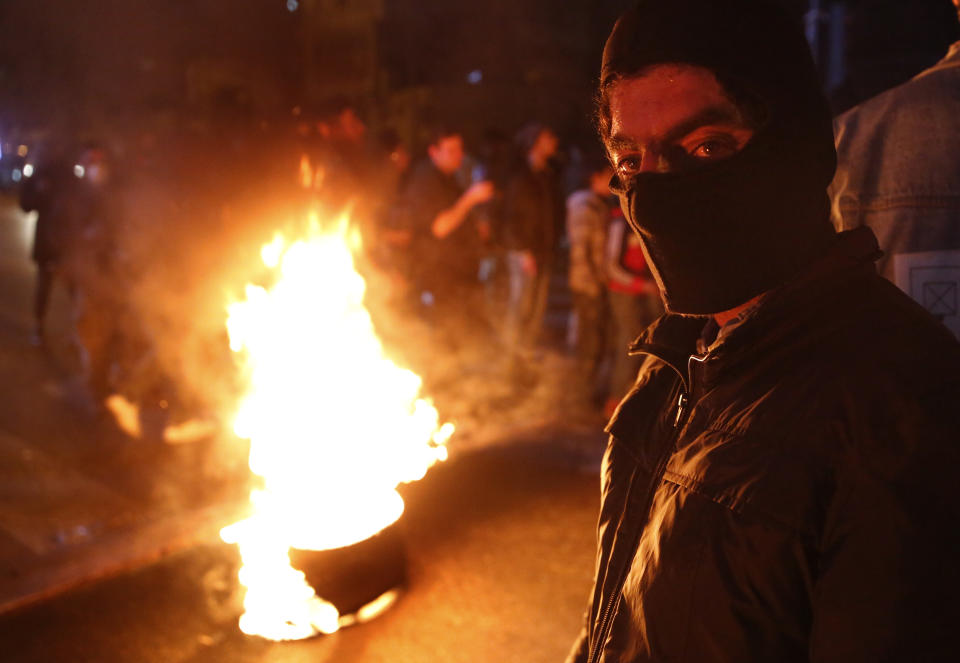An anti-government protester stands next to burning tire during ongoing protests against the country's financial woes, in Beirut, Lebanon, Wednesday, Jan. 15, 2020. Lebanese security forces arrested 59 people, the police said Wednesday, following clashes overnight outside the central bank as angry protesters vented their fury against the country's ruling elite and the worsening financial crisis. (AP Photo/Hussein Malla)