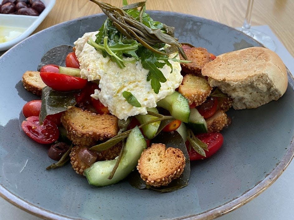 greek meal on a blue/gray plate with a glass of wine