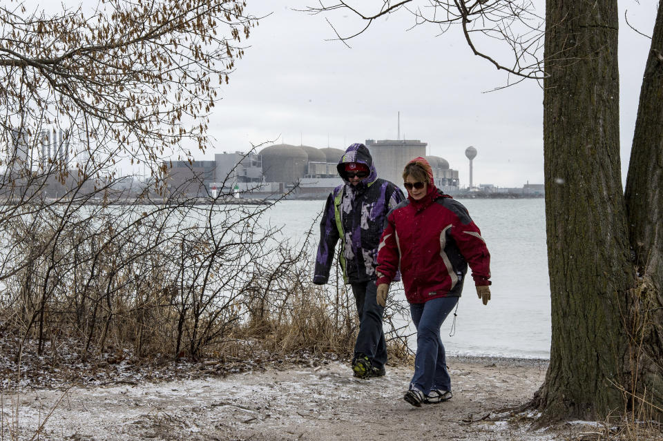 People walk backdropped by the Pickering Nuclear Generating Station in Pickering, Ontario, Sunday, Jan. 12, 2020. The Ontario Power Generation said an alert warning Ontario residents of an unspecified "incident" at the nuclear plant early Sunday morning was sent in error. (Frank Gunn/The Canadian Press via AP)