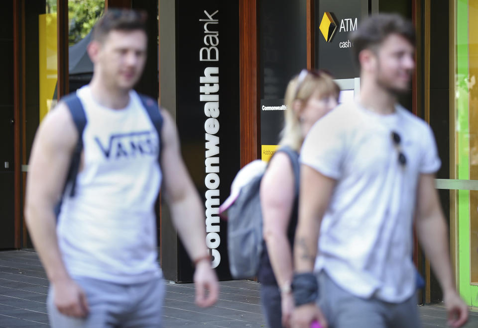 People pass by a Commonwealth Bank ATM in Sydney, Wednesday, Feb. 6, 2019. The Commonwealth Bank of Australia recorded a drop in statutory net profit in its latest half-year to 4.6 billion Australian dollars ($3.3 billion) as the nation's biggest lender was hit by costs for misconduct as well as lower profit margins and a downturn in the housing market. (AP Photo/Rick Rycroft)