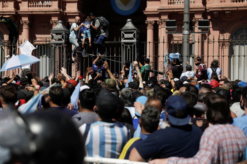 Foto del jueves de dos hombre ayudando a una niña a subir a una valla frente a la Casa Rosada durante el velorio de Diego Armando Maradona