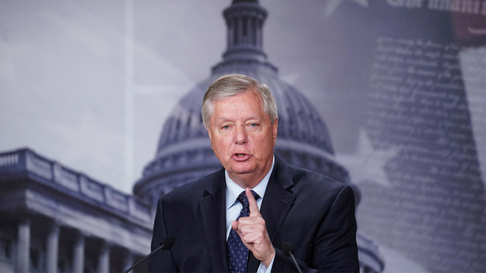 Sen. Lindsey Graham raises his index finger as he speaks in front of a backdrop showing the Capitol.
