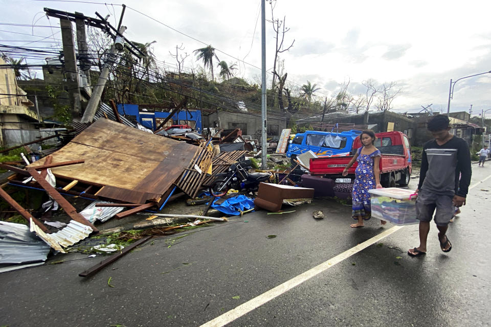 Residents carry what's left of their belongings as they walk past damaged homes due to Typhoon Rai in Surigao city, Surigao del Norte, central Philippines on Friday Dec. 17, 2021. A powerful typhoon left more than a dozen people dead, knocked down power and communications in entire provinces and wrought widespread destruction mostly in the central Philippines, officials said Saturday. (AP Photo/Erwin Mascarinas)