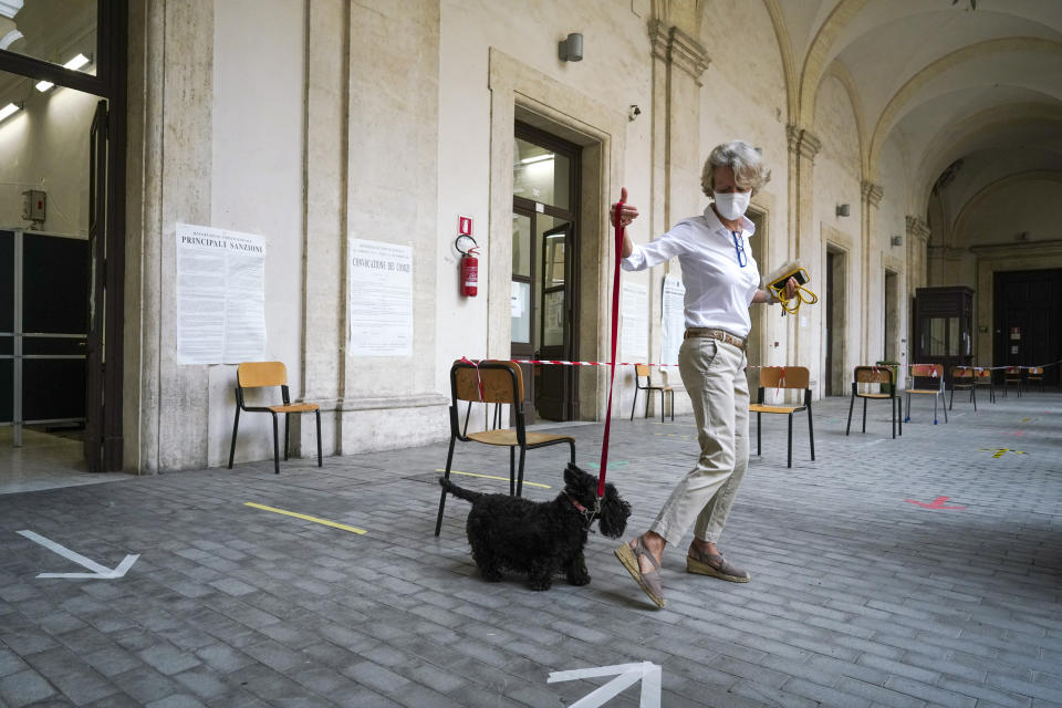 A woman with her dog leaves after voting at a polling station, in Rome, Sunday, Sept. 20, 2020. On Sunday and Monday Italians are called to vote nationwide in a referendum to confirm a historical change to the country's constitution to drastically reduce the number of Members of Parliament from 945 to 600. Eighteen million of Italian citizens will also vote on Sunday and Monday to renew local governors in seven regions, along with mayors in approximately 1,000 cities. (AP Photo/Andrew Medichini)