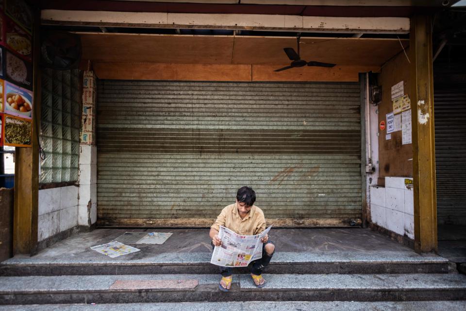 A man reads a newspaper sitting in front of a closed shop during a one-day nationwide Janata (civil) curfew imposed as a preventive measure against the COVID-19 coronavirus, in the old quarters of New Delhi on March 22, 2020. - Nearly one billion people around the world were confined to their homes, as the coronavirus death toll crossed 13,000 and factories were shut in worst-hit Italy after another single-day fatalities record. (Photo by Jewel SAMAD / AFP) (Photo by JEWEL SAMAD/AFP via Getty Images)