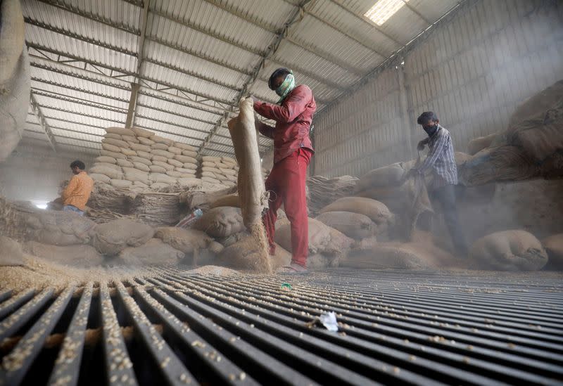 Workers empty wheat sacks for sifting at a grain mill on the outskirts of Ahmedabad