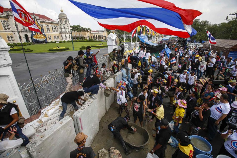 Anti-government protesters mix cement to be used for building a wall to block a gate of the Government House during a rally in Bangkok