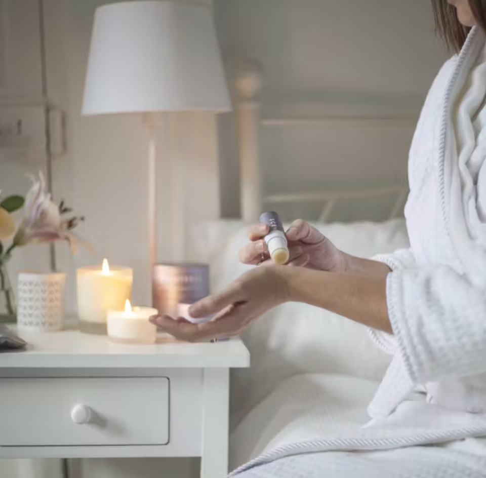 closeup of person in robe sitting in bed and applying balm to wrist