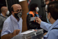 A polling station staff member wears a face mask to help curb the spread of the coronavirus while checking an identity card during the Basque regional election in Durango, northern Spain, Sunday, July 12, 2020. (AP Photo/Alvaro Barrientos)