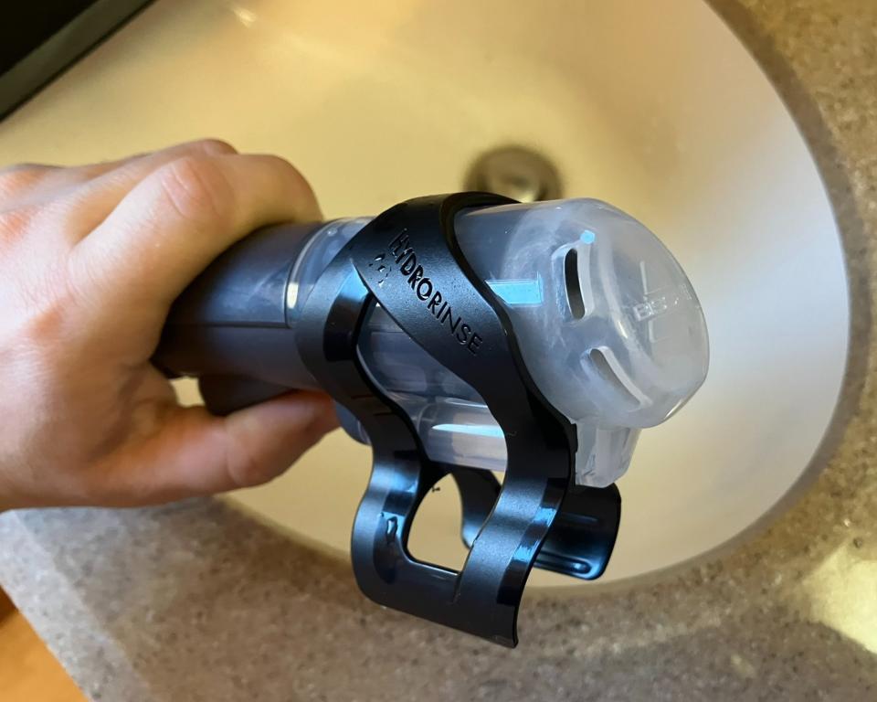 Paige Cerulli, a white woman cleaning the Bissell Little Green Portable Carpet Cleaner, pictured holding the hose over the sink