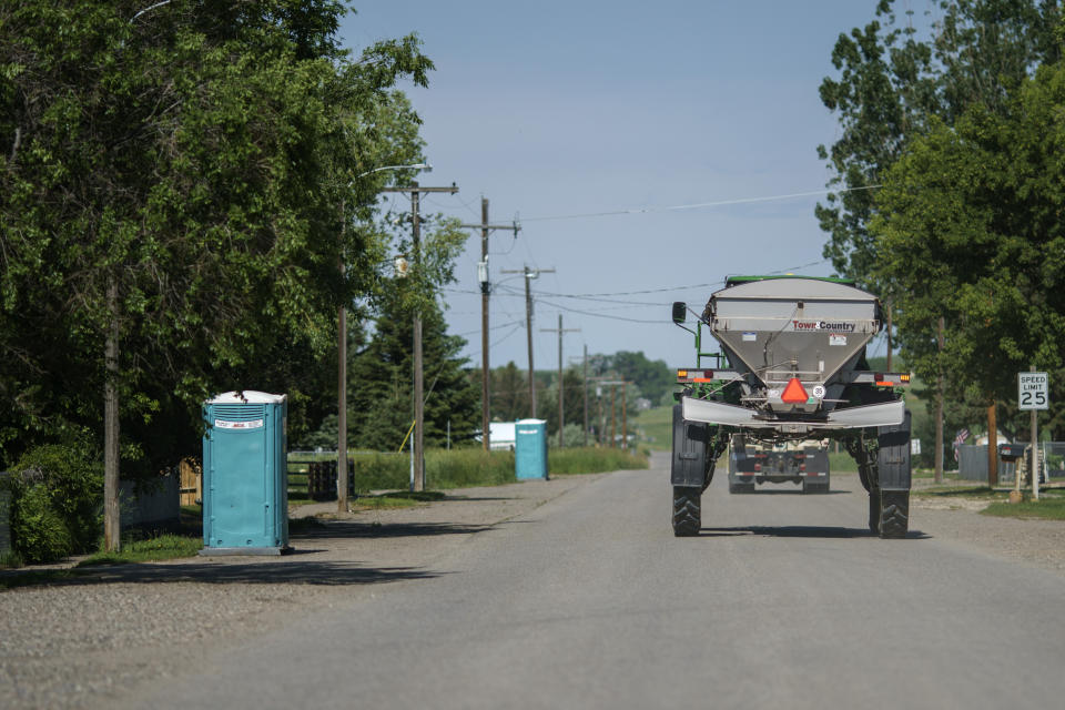 Portable toilets brought in for residents after a sewer line broke during the severe flooding sit outside homes as a tractor passes through Edgar, Mont. Friday, June 17, 2022. (AP Photo/David Goldman)