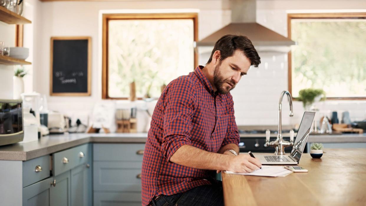 Shot of a handsome man sitting at his kitchen counter with his laptop.