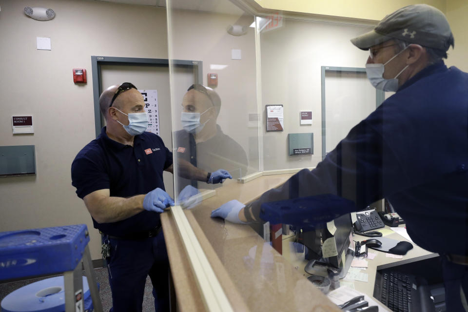 In this Wednesday, May 20, 2020 photo carpenters John Mackie, of Canton, Mass., left, and Doug Hathaway, of Holliston, Mass., right, apply trim to a newly installed plastic barrier in an office area, at Boston University, in Boston. Boston University is among a growing number of universities making plans to bring students back to campus this fall, but with new measures meant to keep the coronavirus at bay. (AP Photo/Steven Senne)