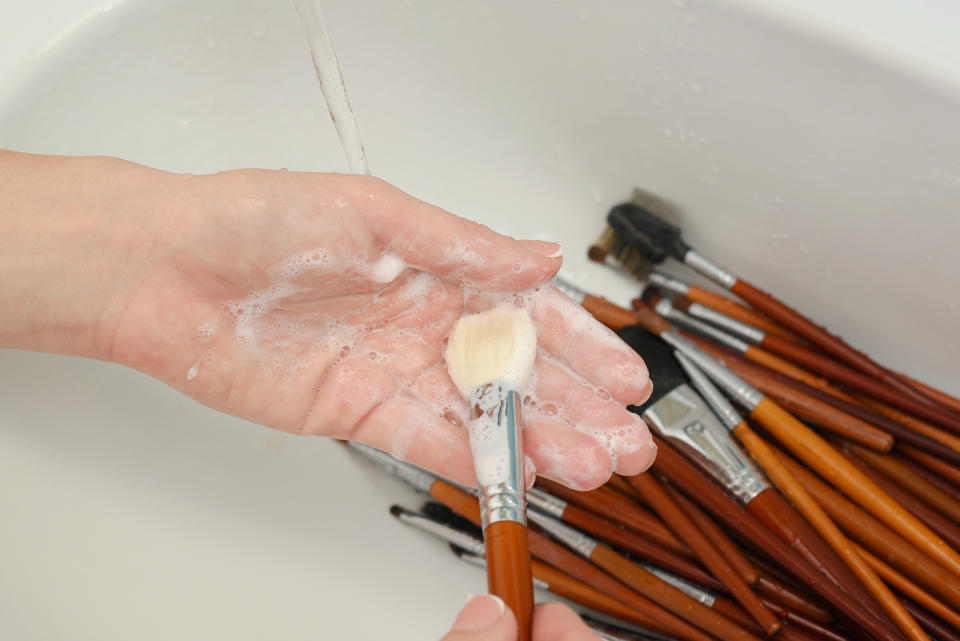 woman washes makeup brushes under running water