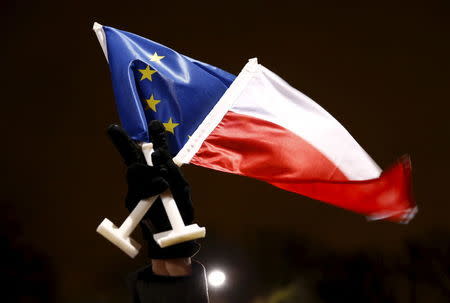 A protester flashes a victory sign as he holds Polish and EU flags during an anti-government demonstration in front of PiS (Law and Justice) leader Jaroslaw Kaczynski's house in Warsaw, Poland December 13, 2015. REUTERS/Kacper Pempel