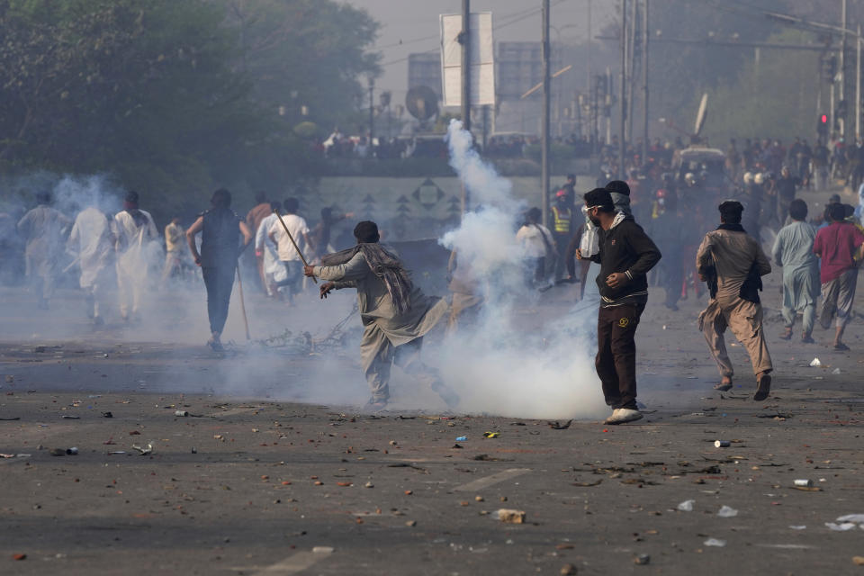 Supporters of former Prime Minister Imran Khan throw stones toward riot police officers firing tear gas to disperse them during clashes, in Lahore, Pakistan, Wednesday, March 15, 2023. Clashes between Pakistan's police and supporters of Khan persisted outside his home in the eastern city of Lahore on Wednesday, a day after officers went to arrest him for failing to appear in court on graft charges. (AP Photo/K.M. Chaudary)