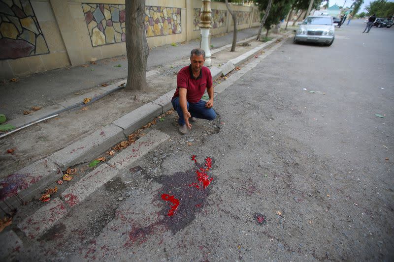 A man points at blood stains on a road in Terter