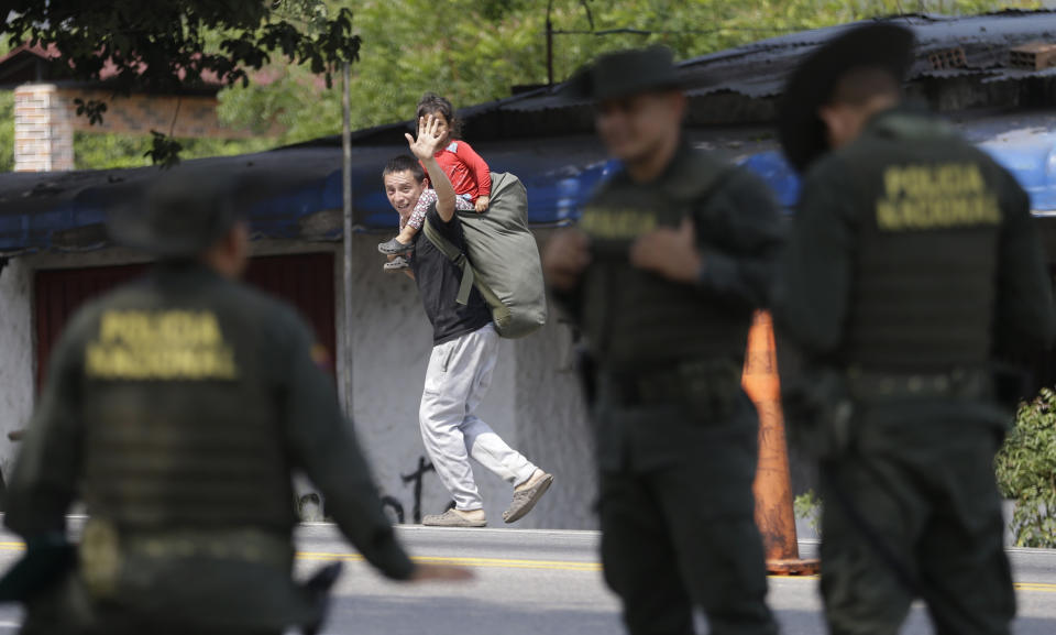 In this Feb. 7, 2019 photo, a Venezuelan migrant waves at Colombian police as he walks past in Los Patios, near Cucuta, Colombia. Humanitarian assistance from the U.S. for Venezuelan over objections from President Nicolas Maduro, has arrived in Cucuta. (AP Photo/Fernando Vergara)