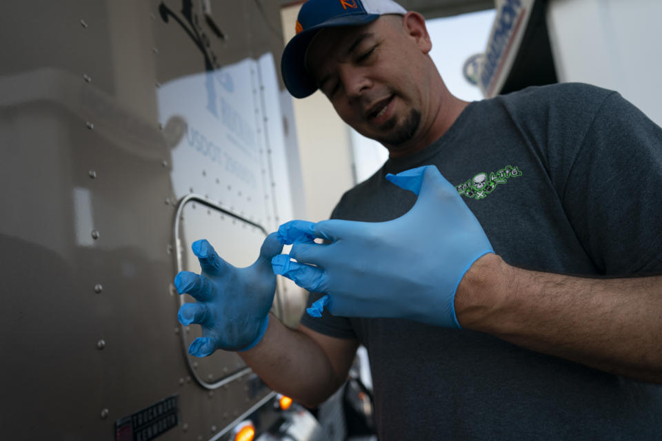 In this April 5, 2020, photo, truck driver Sammy Lloyd, of Ringgold, Ga., struggles to put on surgical gloves to fuel his truck at the Fas Mart in Winchester, Ky. Lloyd wears surgical gloves to protect himself from coronavirus that may contaminate the fuel pumps. Lloyd was pulling a COVID-19 emergency relief load of supplies from California to Virginia. (AP Photo/Carolyn Kaster)