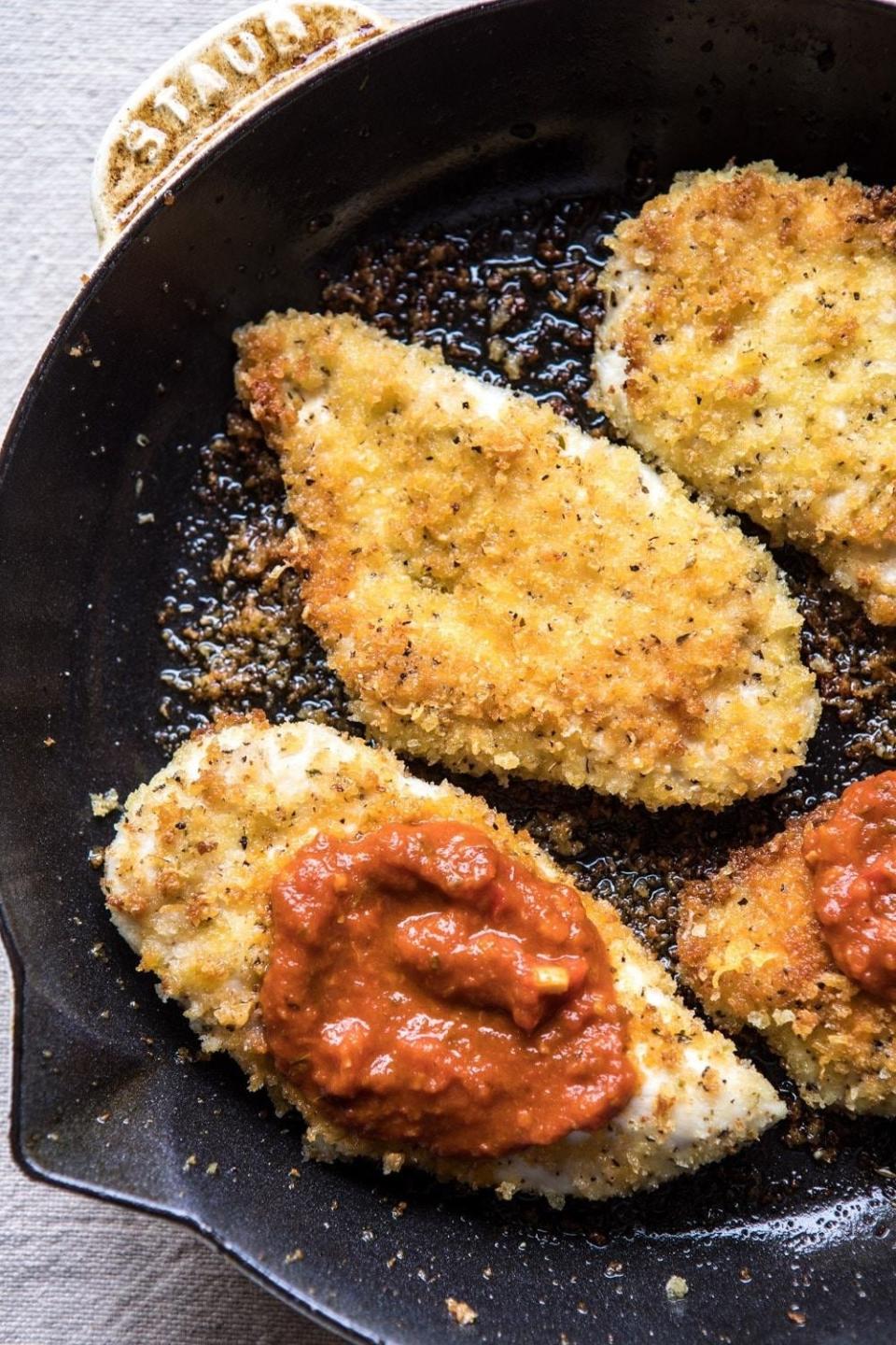 Breaded chicken cutlets in a pan with a dollop of tomato sauce