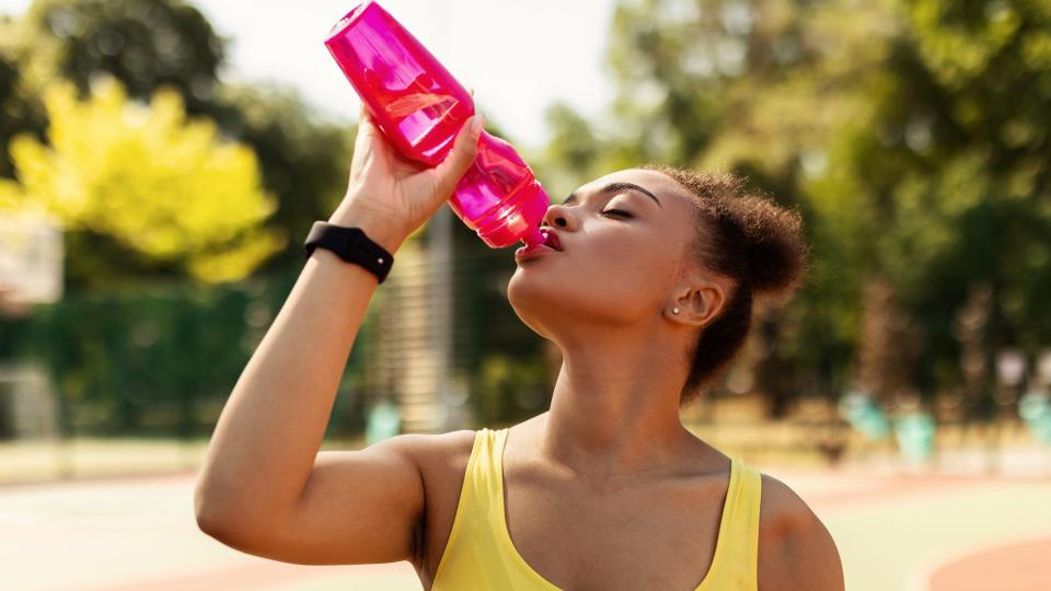 Portrait of sporty black woman in yellow top drinking water