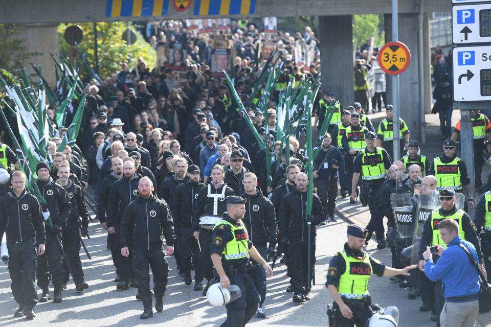 Protesters march in narrow rows as police stand on the sidelines.