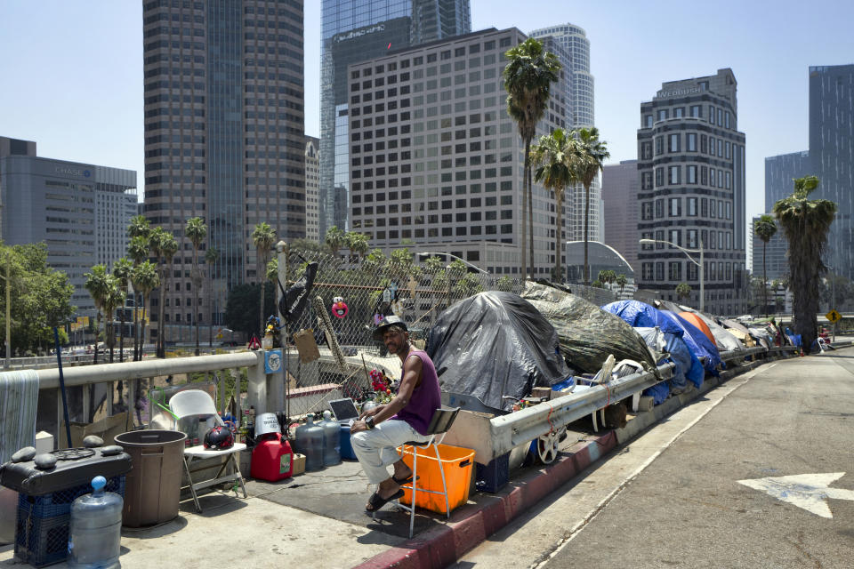 FILE - In this May 10, 2018 file photo, a homeless person sits at his tent along the Interstate 110 freeway downtown Los Angeles. Mayor Eric Garcetti is paying a political price for the city's homeless crisis. An effort is underway to recall the two-term Democrat from office prompted by widespread complaints about homeless encampments throughout the city. Figures released earlier this month showed a 16% jump in LA's homeless population over the last year, pegging it at 36,300, the size of a small city. (AP Photo/Richard Vogel, File)