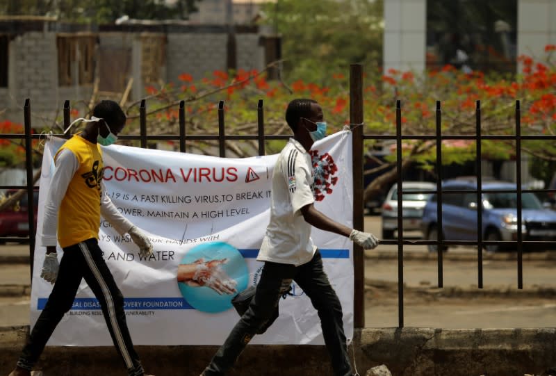 Two men with protective face mask walks past a poster at Wuse market, as the authorities try to limit the spread of coronavirus in Abuja