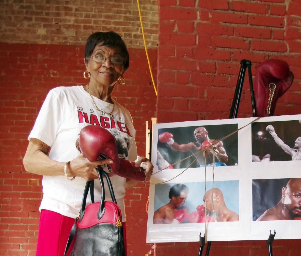 Mae Lang, of Brockton, mother of the late great middleweight boxing champion Marvelous Marvin Hagler, and dressed in Brockton colors, stands next to pictures of her son with one of his boxing gloves at the location of the former Petronelli Gym on Monday, April 4, 2022, where Marvelous Marvin Hagler trained throughout his career.