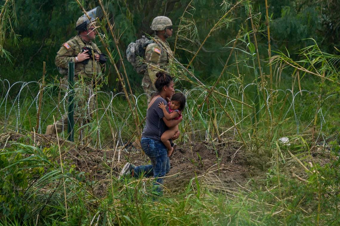 Texas National Guardsmen stand along a stretch of razor wire as a migrant woman carrying a child tries to cross into the U.S, on the banks of the Rio Grande, as seen from Matamoros, Mexico, Thursday, May 11, 2023. Migrants rushed across the Mexico border Thursday in hopes of entering the U.S. in the final hours before pandemic-related asylum restrictions are lifted. (AP Photo/Fernando Llano)